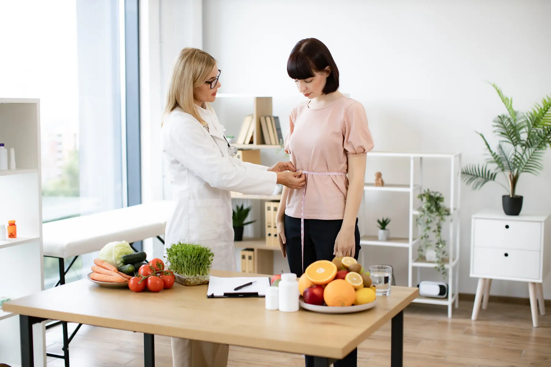 Una nutricionista mide la cintura de una paciente en una consulta luminosa